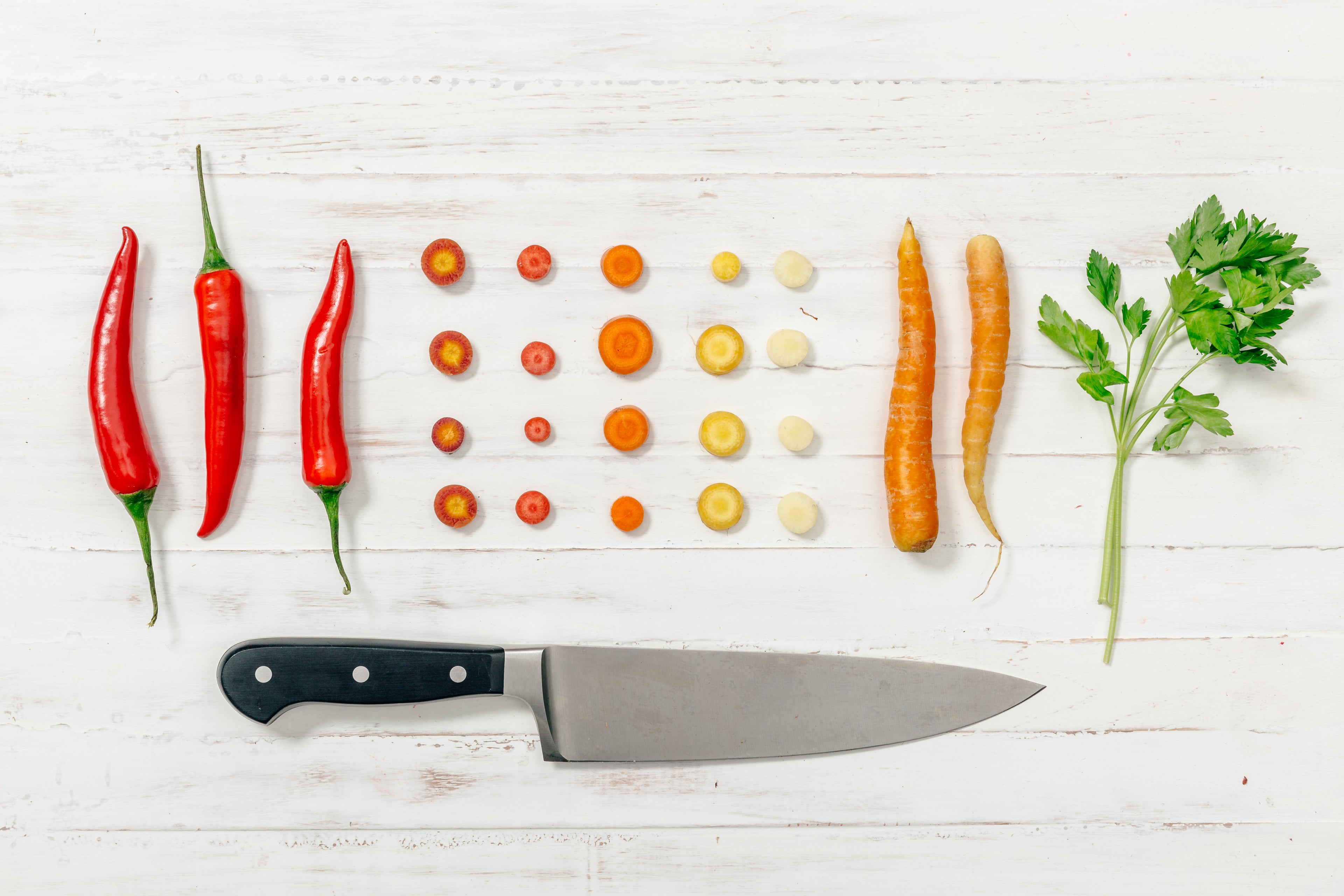 Cut vegetables flat on a white wooden surface with a chef knife below